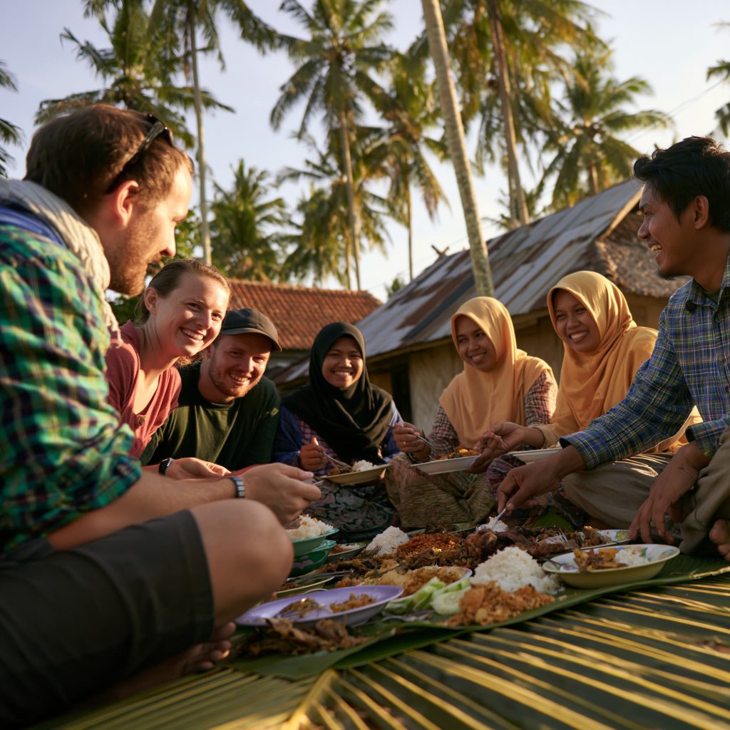 Guests and hosts eating together around a banana leaf at golden hour