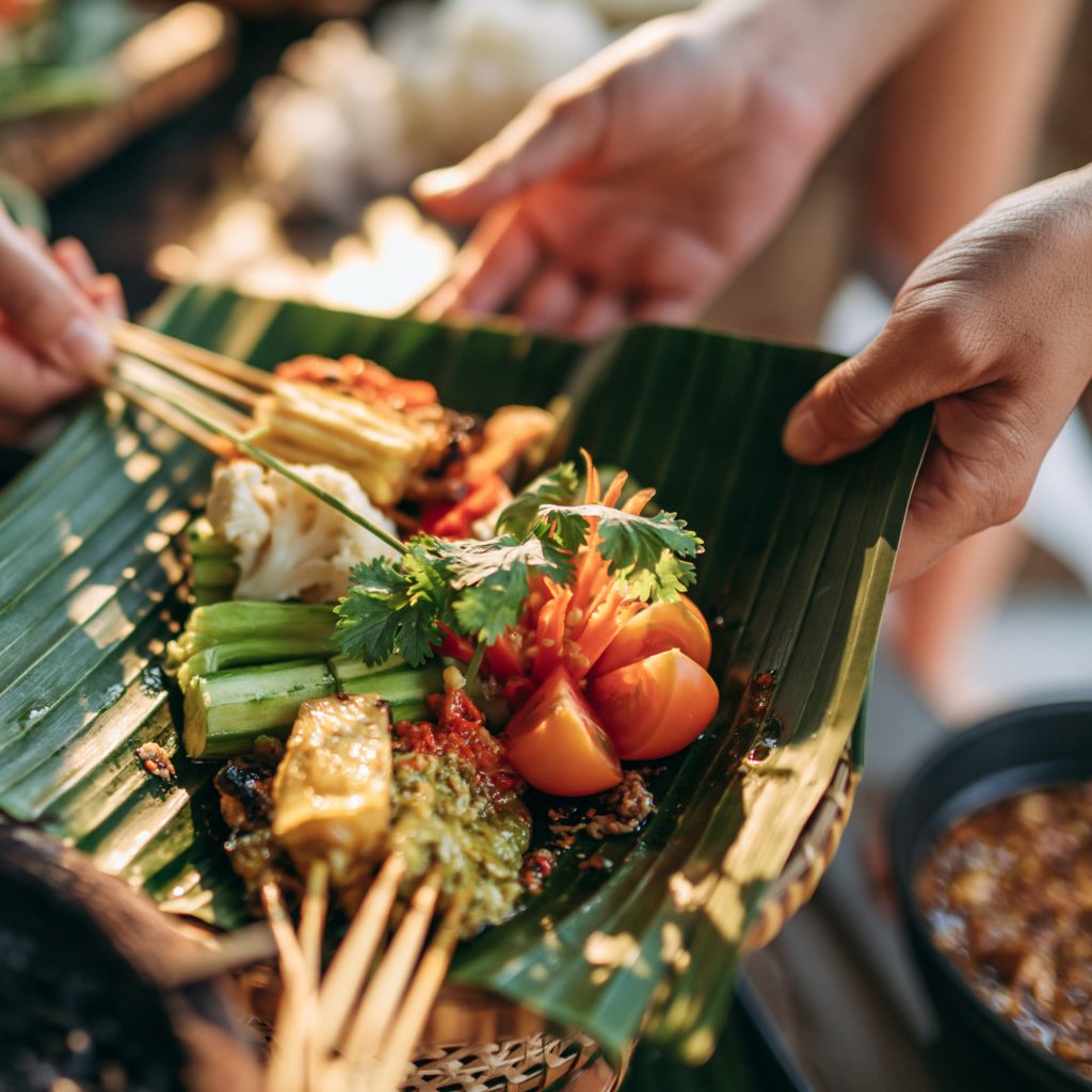 Satay skewers and grilled vegetables served on a banana leaf