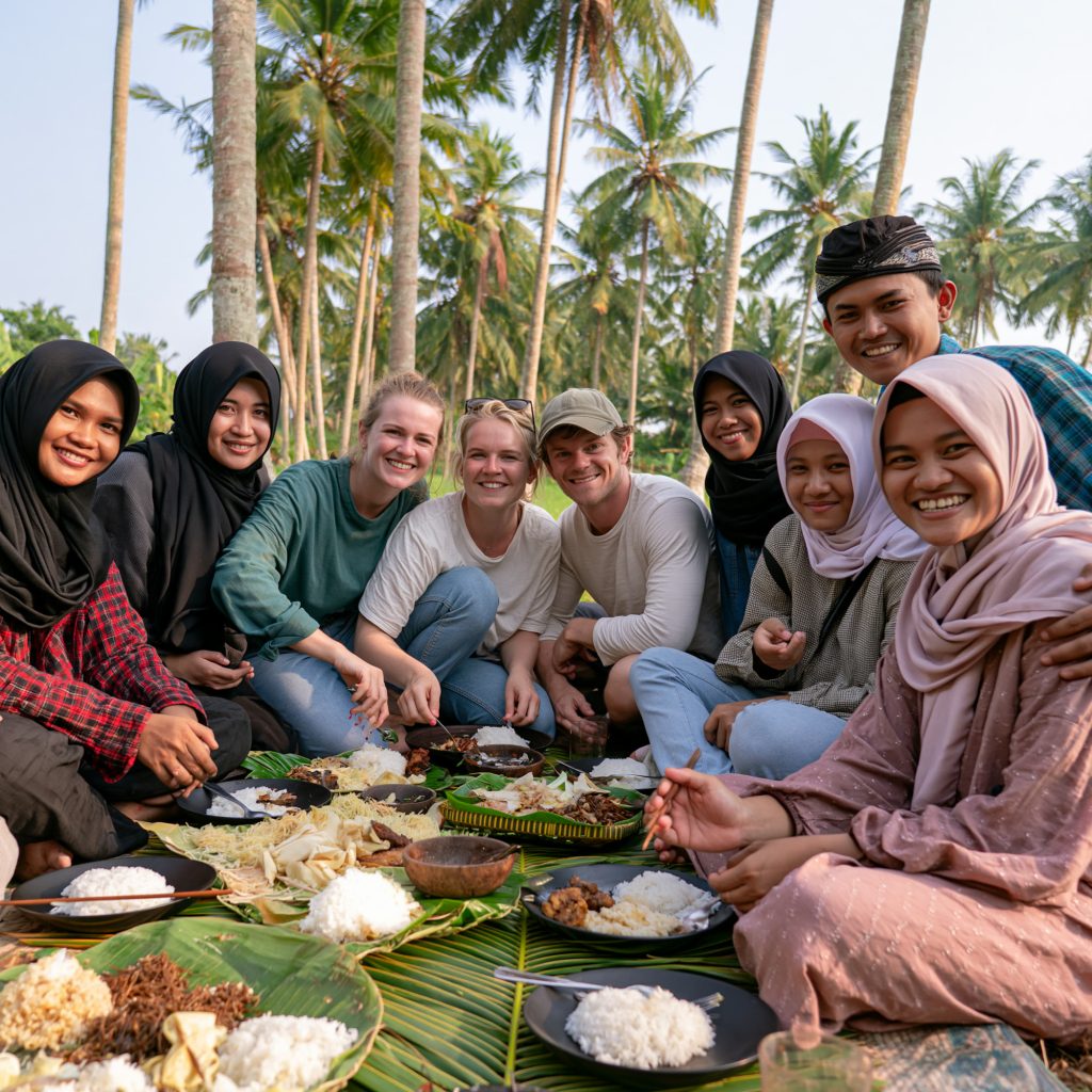 A group sharing a meal on banana leaves beneath coconut palms