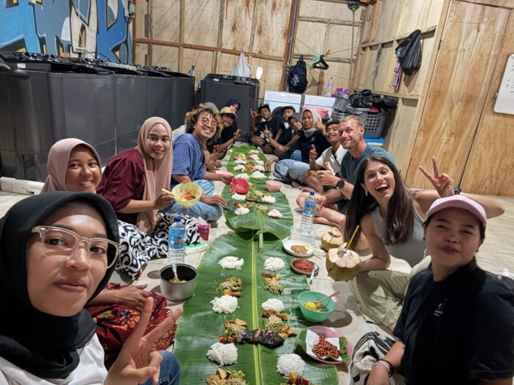 Guests and their host family sitting around a banana leaf laid with rice and Indonesian dishes, Gili Trawangan
